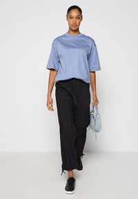 Jasnoniebieski t-shirt z krótkim rękawem, luźny krój; czarne luźne spodnie ze sznurkiem; mała jasnoniebieska torba; czarne trampki. Prosty i nowoczesny design.