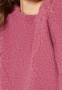 Pull rose tricoté avec un motif en losange texturé, un col côtelé et un tissu doux. Vue en gros plan mettant en valeur les détails et la texture.