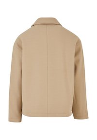 Veste beige à manches longues avec un col droit, une couture centrale visible dans le dos, et une coupe légèrement ample.