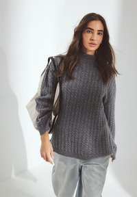 Pull en maille grise, en matière douce, avec un col montant et des manches longues, porté avec un jeans en denim clair et un sac tote beige.