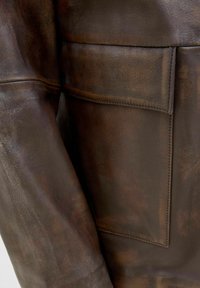 Brown leather jacket with a textured finish, featuring a large front pocket and visible stitching along the seams.
