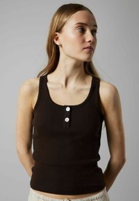 Bruine geribbelde tanktop met een ronde halslijn, gegolfde randen en drie witte knopen in het midden.