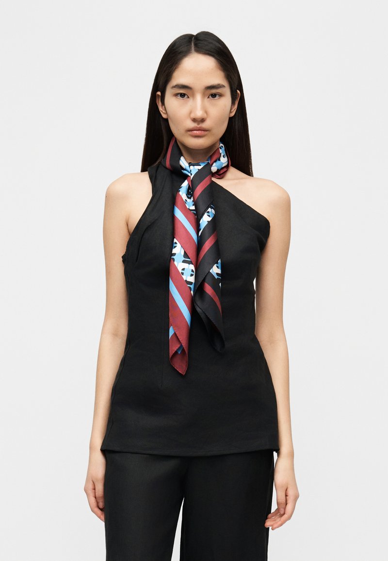 Μαύρο τοπ με λαιμόκοψη halter και ασύμμετρο ντεκολτ έ, συνδυασμένο με πολύχρωμο μεταξωτό φουλάρι με ρίγες σε μπλε και κόκκινο.