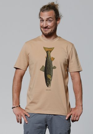 Beige Baumwoll-T-Shirt mit einer detaillierten Fischillustration in Grün und Gelb und Text darunter, getragen von einer Person vor einem neutralen Hintergrund.