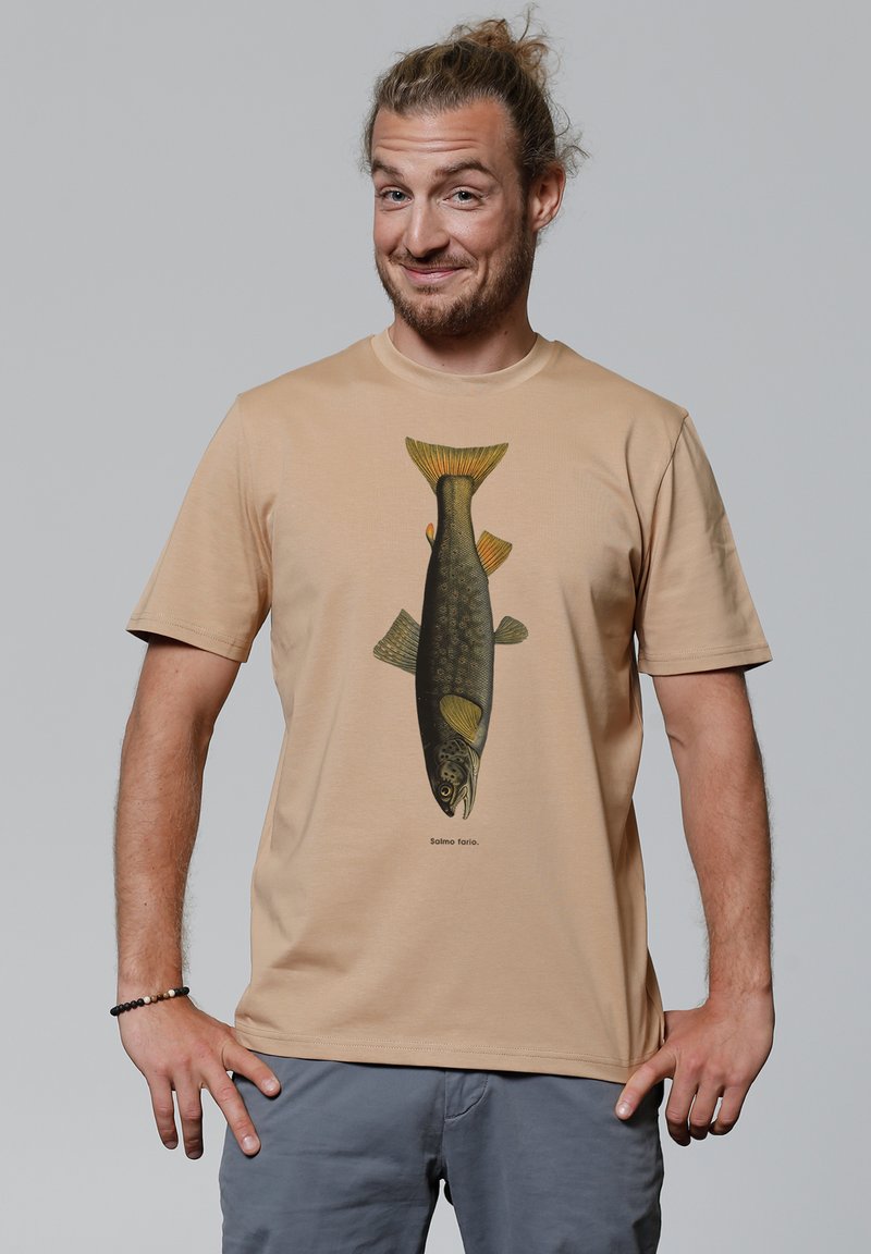 Beige katoenen t-shirt met een gedetailleerde vissenillustratie in groen en geel, met tekst eronder, gedragen door een persoon tegen een neutrale achtergrond.