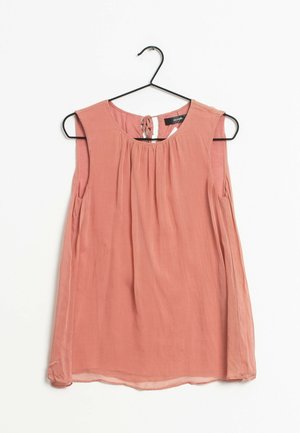 Blouse sans manches de couleur pêche avec un col noué, un devant froncé et une texture fluide. Accrochée sur un cintre noir sur fond blanc.