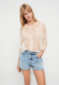 Hosszú ujjú csipkeblúz törtfehér színben, gombos záródással, világoskék farmer sorttal párosítva, mely szakadt szegéllyel és oldalzsebekkel rendelkezik.