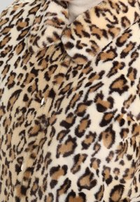 Umělé kožich s hnědým a černým leopardím vzorem nošený přes béžový rolák.