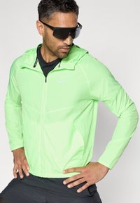 Ελαφρύ, φούτερ μπουφάν σε νεόν πράσινο χρώμα με φερμουάρ και πλαινές τσέπες. Διαθέτει ένα μικρό λευκό λογότυπο στο στήθος και ελαστικές μανσέτες.