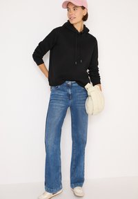 Sudadera negra con cordones; jeans acampanados de color azul claro; bolso cruzado crema; gorra rosa clara; calzado casual.