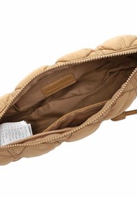 Intérieur d'un sac à main beige matelassé avec doublure en tissu marron, poche zippée et étiquette. Texture douce et moelleuse avec un détail de fermeture éclair lisse.