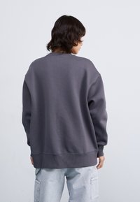 Grijze oversized sweatshirt met een geribbelde ronde hals en boorden, met een zachte textuur. Draagt met lichtgekleurde cargobroeken.