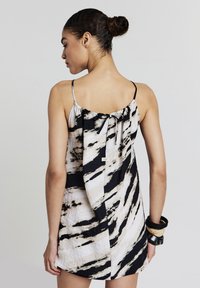 Robe sans manches avec un imprimé abstrait noir et crème, présentant un dos froncé avec un détail à nouer et un ourlet courbé.