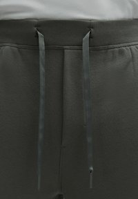 Sötét szürke sportnadrág, texturált anyagból, lapos derékpánttal és hozzá illő húzózsinórral, fém végződésekkel a beállításhoz.