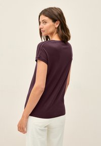 Kortärmad, rundhalsad t-shirt i mörklila bomull. Har uppvikta ärmar och en avslappnad passform. Bärs med ljusa byxor.