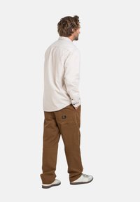 Light beige long-sleeve shirt with button cuffs paired with brown cargo pants featuring pockets. Gray and white sneakers complete the outfit.