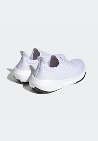 Witte sportschoenen met een getextureerde bovenkant, gewatteerde hiel en een dikke witte tussenzool met een zwarte buitenzool. Drie accentstrepen aan elke kant.