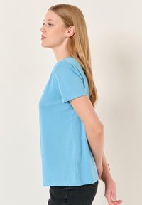 Jasnoniebieska koszulka z krótkim rękawem wykonana z gładkiego materiału, o luźnym kroju i prostym okrągłym dekolcie, bez widocznych wzorów czy akcentów.