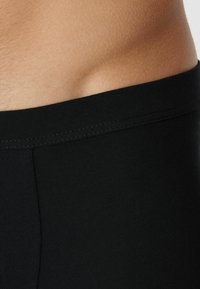 Czarne bawełniane slipki o gładkiej fakturze i elastycznym pasku, pokazujące tylko częściowy widok odzieży i przylegającej skóry.