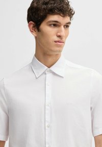 Camicia bianca a maniche corte realizzata in tessuto leggero, con colletto button-down e un piccolo logo ricamato sul petto.