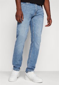 Světle modré denimové džíny se stříháním rovného nohavic, předními kapsami a jemným vyblednutím. V kombinaci s bílými sportovními botami.