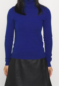 Blå polotröja i mjukt tyg med långa ärmar, kroppsnära passform och ribbade ärmslut och fåll, kombinerad med en svart läderkjol.