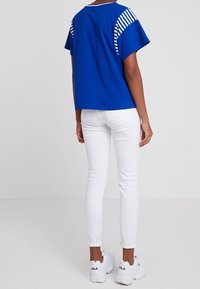 Blue cotton t-shirt with striped accents on the sleeves, paired with white skinny jeans and white sneakers. Back view displayed.