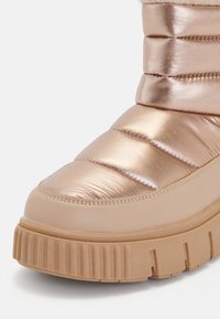 Nafúknutá kovová krištáľovo zlatá čižma s hladkým, lesklým zvrškom, mäkkou podšívkou a hrubou, zúbkovanou gumovou podrážkou.