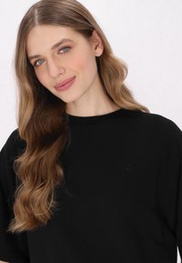 Musta collegepaita, jossa on pyöreä kaula-aukko ja lyhyet raglan-hihat. Sisältää pienen ankkurilogon hienovaraisessa, sopivassa värissä.