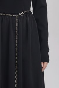 Svart kjole med lange ermer, samlet midje og sølvkjede belte. Glatt tekstur med en flytende skjørt og tettsittende liv.