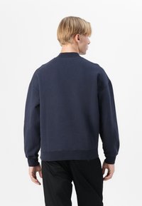 Tengerészkék pulóver, laza szabással, kerek nyakkivágással és hosszú ujjal. Puha anyagból készült, bordás mandzsettával és alsó szegéllyel.