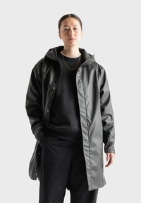 Gray waterproof raincoat with a hood, snap buttons, and a relaxed fit, layered over a black sweater and pants. Smooth, shiny texture.
