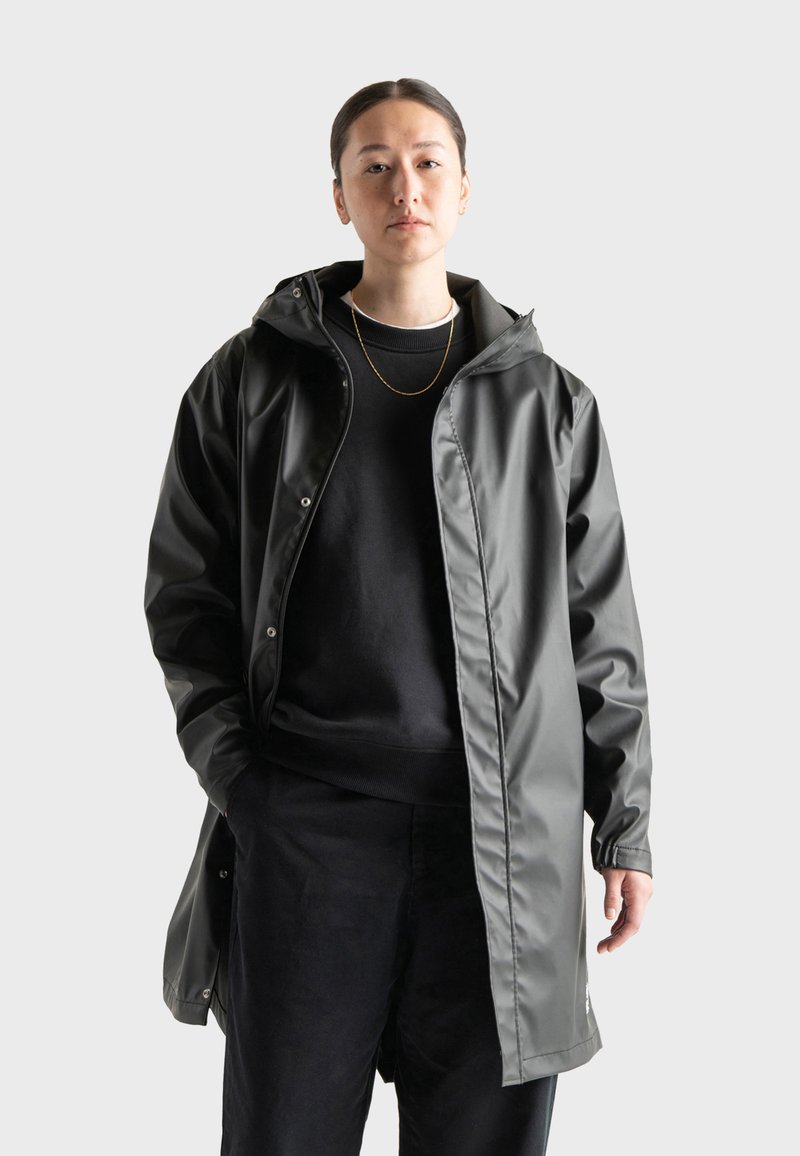 Gray waterproof raincoat with a hood, snap buttons, and a relaxed fit, layered over a black sweater and pants. Smooth, shiny texture.