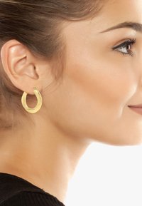 Orecchini a cerchio in oro con una finitura liscia e lucida, caratterizzati da un design aperto e curvo e una piccola pietra di accento nella parte superiore.