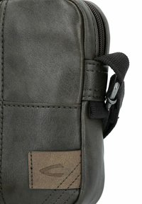 Dunkelgrüne Lederhandtasche mit Reißverschluss, strukturiertem Oberflächenmaterial, genähten Akzenten und einem kleinen braunen Logopatch an der Seite.