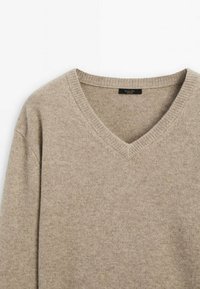 Pull en laine beige col V avec col côtelé et couture d'épaule visible, avec une petite étiquette de marque noire à l'intérieur du col.
