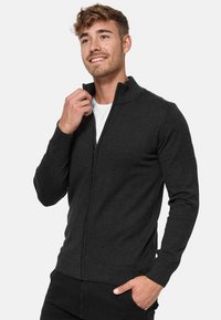 Zwartgrijze zip-up sweater met een hoge kraag, ribbelmanchetten en zoom, gemaakt van een gladde, gestructureerde stof. Gevoerde rits detail aan de voorkant.