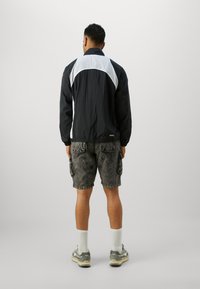 Black and white windbreaker with a textured finish, featuring an elastic hem and cuffs; paired with gray cargo shorts and sneakers.