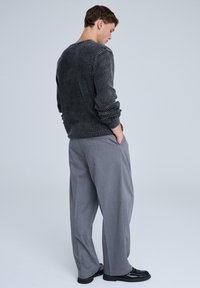 Maglione nero lavorato a maglia con coste verticali, abbinato a pantaloni a gamba larga grigio chiaro e mocassini neri. Modello visto da dietro.