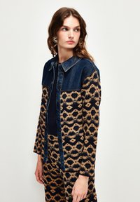 Jeansjacka med ett mönstrat nedre parti i beige och marinblått, med krage, knappstängning och långa ärmar.