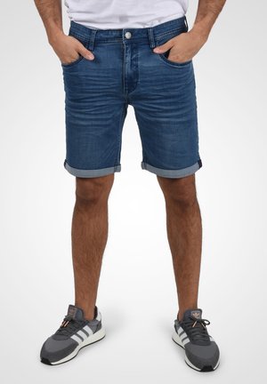 Shorts en denim bleu foncé, avec un ourlet retroussé et un design à cinq poches, accompagnés de chaussures de sport légères grises.