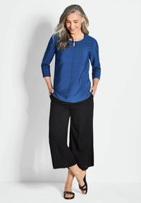 Blusa blu a maniche a tre quarti con scollatura a chiave, abbinata a pantaloni neri a gamba larga e sandali neri, con una texture liscia.
