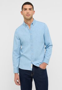 Jasnoniebieska koszula dżinsowa z kołnierzykiem zapinanym na guziki, długimi rękawami i guzikami z przodu. Noszona z ciemnymi dżinsami; subtelna faktura i swobodny design.