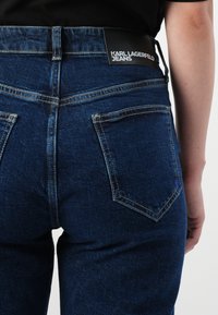 Tamsiai mėlynos džinsinės kelnės su tiesiu siluetu, su juodu žymeniu "KARL LAGERFELD JEANS", dviem užpakalinėmis kišenėmis ir kontrastingais siūlais.