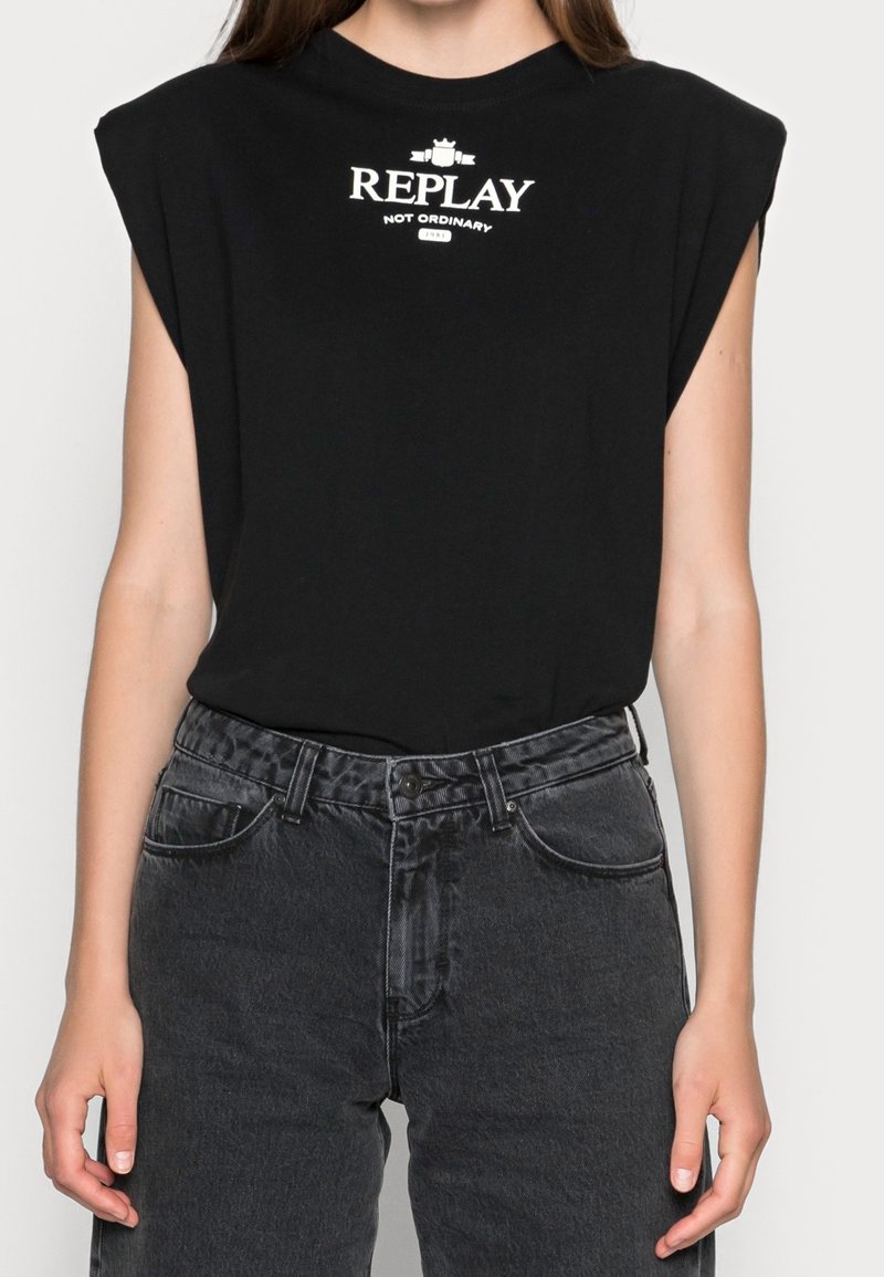 Czarna krótki rękaw t-shirt z poduszkami na ramionach, z białym logo, które brzmi "REPLAY NOT ORDINARY", w połączeniu z ciemnoniebieskimi dżinsami o wysokim stanem.