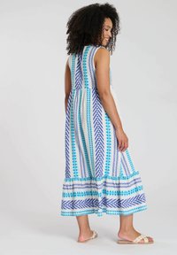 Maxi-jurk met een mouwloos ontwerp, witte stof met blauwe en turquoise geometrische patronen, en een geraffineerde taille met een gerimpelde zoom.
