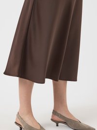 Saia midi castanha em tecido liso, com um formato evasê e um suave brilho; combinada com sapatos slingback cinza claro com pequenos saltos.