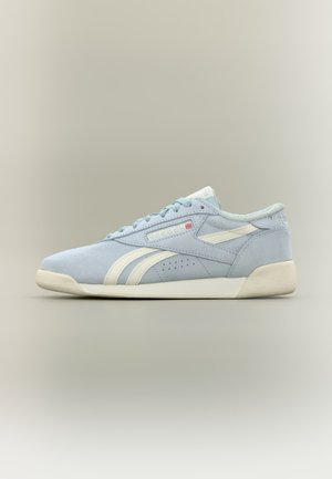 Basket Reebok bleu clair avec des bandes blanches, semelle blanche et lacets, présenté sur un fond beige neutre.