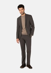 Grauer Anzug mit schmaler Passform, einreihiger Blazer und passende Hose. Getragen über einem hellbraunen Rundhals-Pullover und braunen Schuhen.