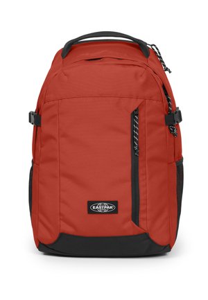 Red fabric backpack with a black base, featuring side pockets, a zippered front, and a logo patch. Adjustable straps and top handle included.